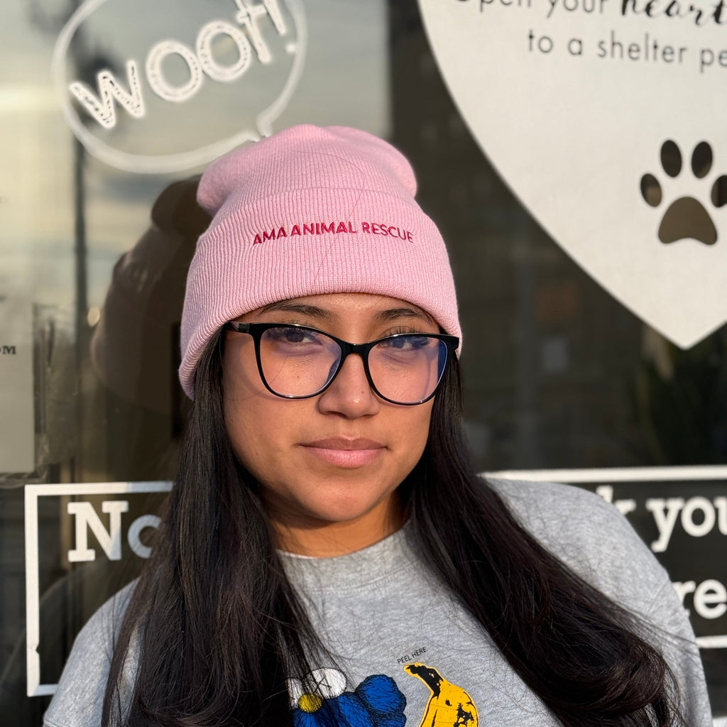 Person wearing a pink beanie with 'AMA Animal Rescue' and a gray sweatshirt with a blue and yellow design, standing in front of AMA Animal rescue in brooklyn