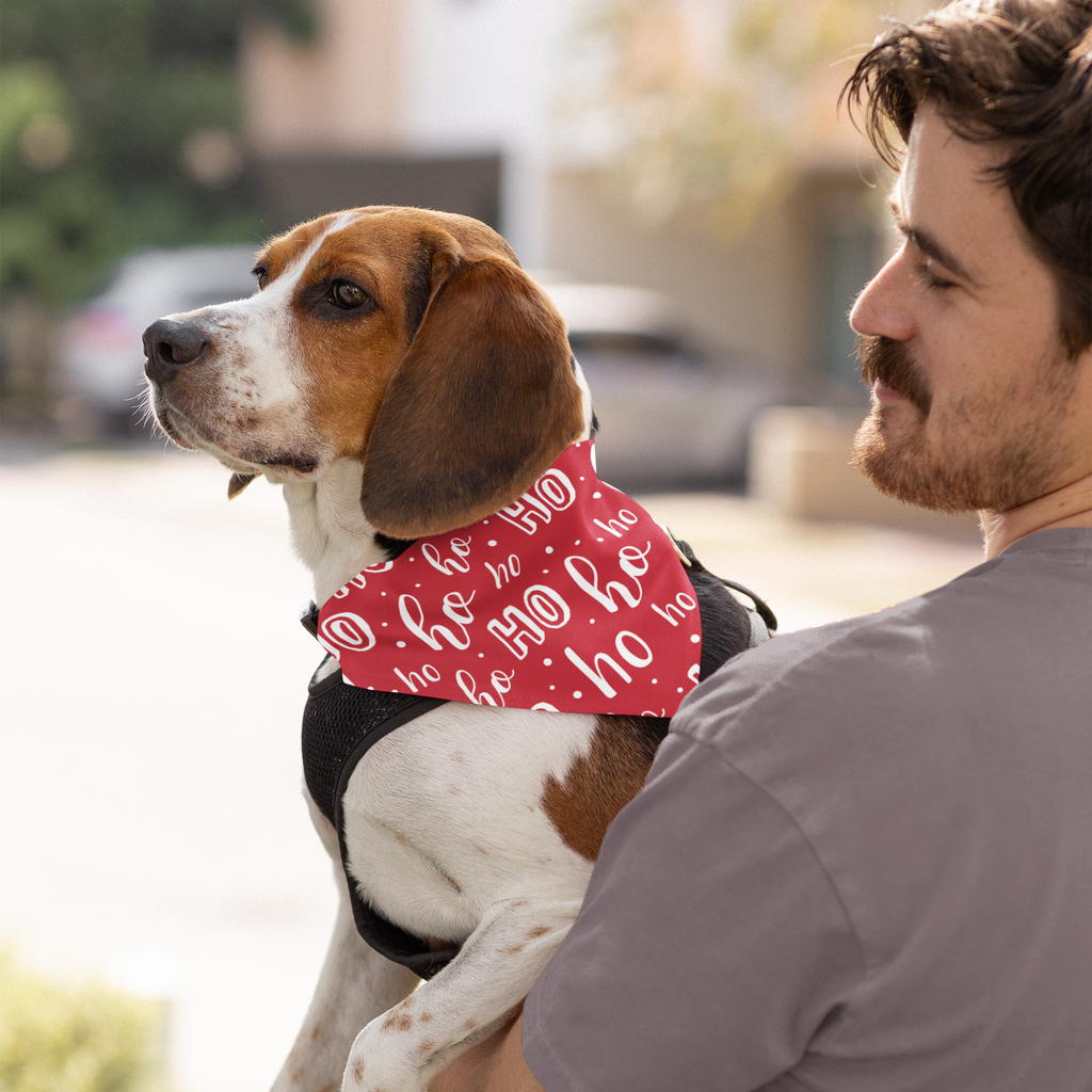 Man holding a dog wearing a red bandana with white text in an outdoor setting